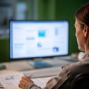 Healthcare operations manager reviewing migration reports beside a desktop monitor in a quiet office